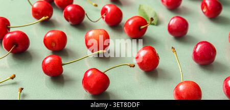 Fresh red cherries with stems scattered on a light green background, healthy fruit and summer harvest Stock Photo