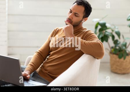 Young Man Thinking While Using Laptop In Modern Home Office, Business Concept Stock Photo