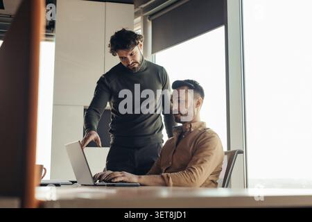 Two Men Collaborating In Office, One Pointing At Laptop Screen, Business Concept Stock Photo