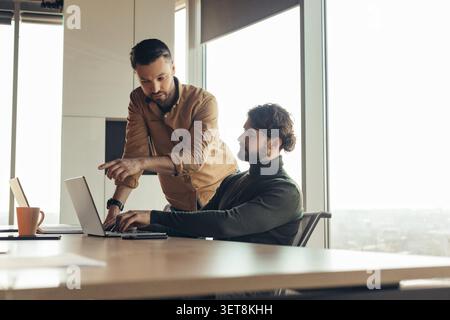 Two Men Collaborating In Office, Focused On Laptop, Business Concept Stock Photo