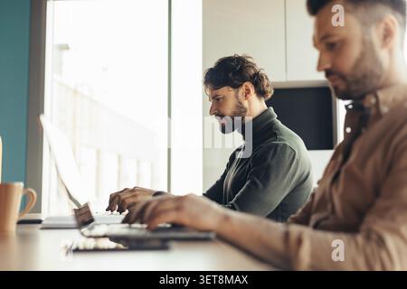 Two Men Working Intently On Laptops In Modern Office, Business Concept Stock Photo