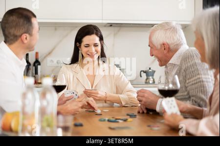 Joyful senior parents and young couple sitting around table playing poker Stock Photo