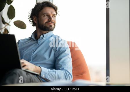 Thoughtful Man With Beard Working On Laptop In Modern Office, Business Concept Stock Photo