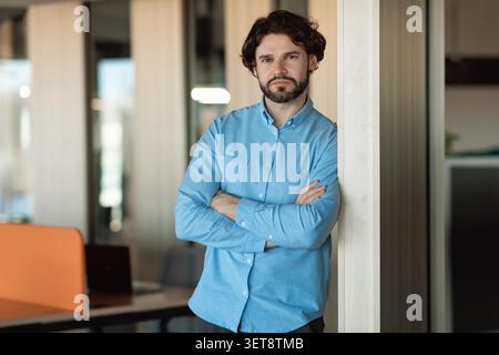 Confident Caucasian Man Leaning Against Wall With Arms Crossed, Office Setting, Business Concept Stock Photo