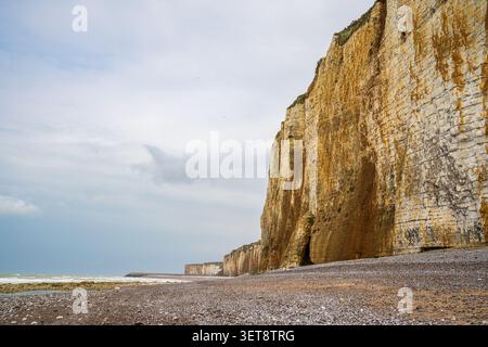 A close-up view showcases majestic layered cliffs with warm ochre and golden tones. At the foot of the rock wall, the pebble beach stretches out, lapp Stock Photo