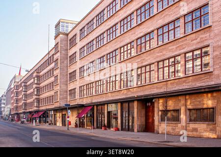 An angled shot shows the long stone facade of a building with repeating, geometric rows of windows. The ground floor features wooden entrances, storef Stock Photo