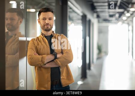Confident Caucasian Man Standing In Modern Office, Arms Crossed, Business Concept Stock Photo
