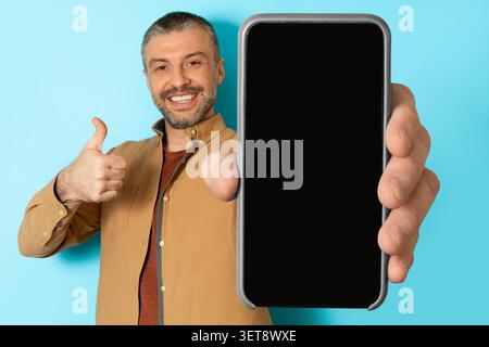Smiling Caucasian Man Holding Smartphone With Blank Screen, Indoor Setting, Technology Concept Stock Photo