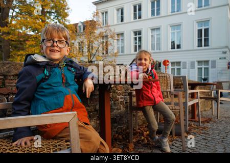 Two children sit at outdoor cafe seating in autumn town bridge Stock Photo