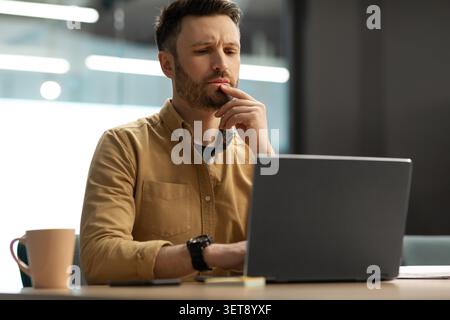 Focused Young Caucasian Man Working On Laptop In Office, Business Concept Stock Photo