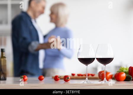 Unrecognizable Elderly Couple Dancing Together In Cozy Kitchen With Red Wine And Fresh Tomatoes Stock Photo