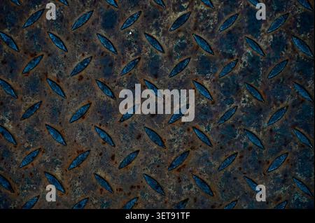 ​A beautiful horizontal macro shot capturing the gritty texture of a dark, weathered diamond plate metal sheet. Stock Photo