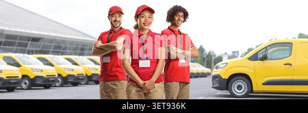 Group of delivery workers in red uniforms standing in front of yellow vans Stock Photo