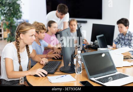 Portrait of teen schoolgirl sitting at table in computer class during lesson, smiling at camera. Concept of teenagers and technologies Stock Photo