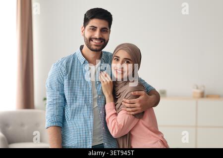 Happy Young Couple Smiling Together At Home, Embracing In Cozy Living Room Stock Photo