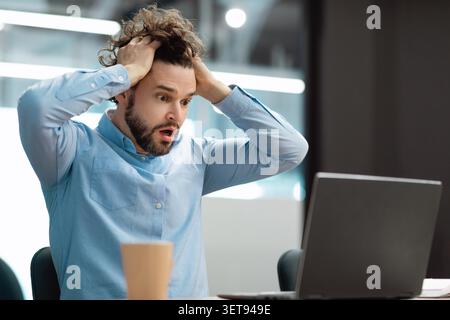Worried Man Holding Head In Office While Using Laptop, Stress Concept Stock Photo