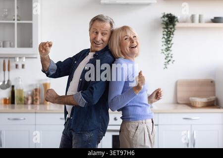 Happy Elderly Caucasian Couple Dancing Together At Home In Kitchen, Joyful Moment Stock Photo