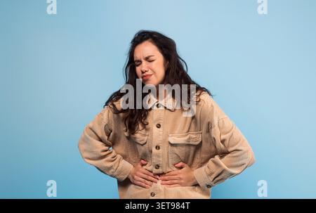 Young Woman Holding Stomach With Discomfort, Upset Expression, Healthcare Concept Stock Photo