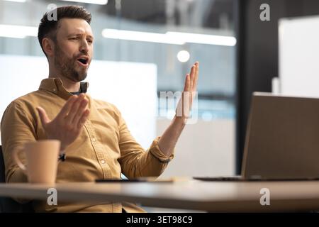 Frustrated Man Gesturing While Working On Laptop In Office, Business Concept Stock Photo