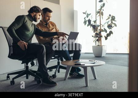 Two Men Collaborating On Laptop In Modern Office, Focused Business Concept Stock Photo