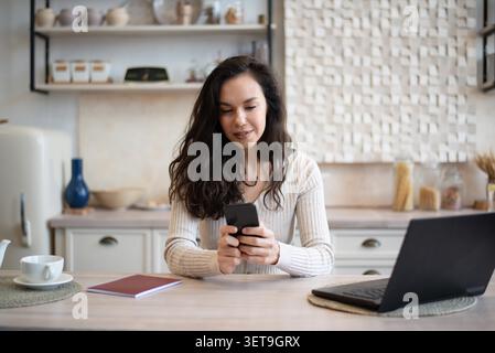 Young Woman Using Smartphone And Laptop At Home Office, Focused, Business Concept Stock Photo