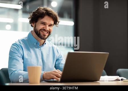 Smiling Young Caucasian Man Working On Laptop At Modern Office, Business Concept Stock Photo
