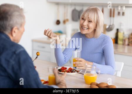 Happy Elderly Caucasian Woman Enjoying Meal With Male Companion At Home, Kitchen Lifestyle Stock Photo