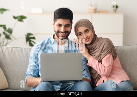 Happy Young Middle Eastern Couple Using Laptop Together In Cozy Living Room Stock Photo