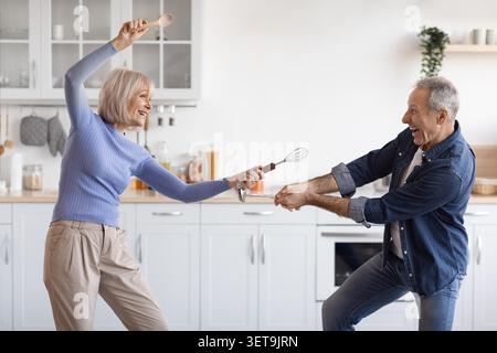 Happy Elderly Couple Cooking Together In Kitchen, Enjoying Fun Cooking Moment Stock Photo