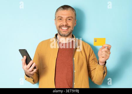 Smiling Middle Aged Caucasian Man Holding Smartphone And Yellow Card, Business Concept Stock Photo