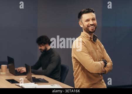 Smiling Young Caucasian Man Standing With Arms Crossed In Modern Office, Business Concept Stock Photo