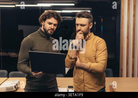Two Men Analyzing Data On Laptop In Office, Focused Expression, Business Concept Stock Photo