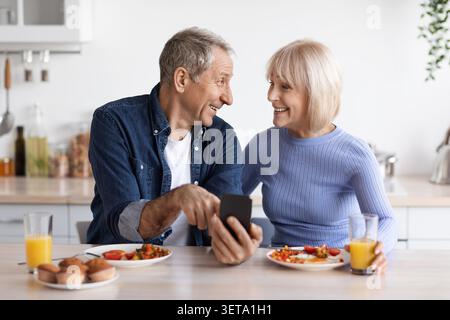 Happy Elderly Caucasian Couple Eating Breakfast Together At Home, Sharing Moment Stock Photo