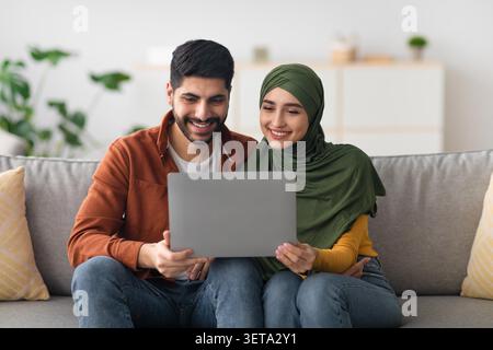 Happy Young Muslim Couple Using Laptop Together At Home, Family Concept Stock Photo
