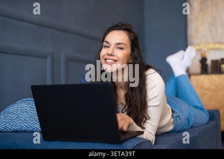 Smiling Young Woman Working On Laptop At Home, Cozy Atmosphere, Remote Work Concept Stock Photo