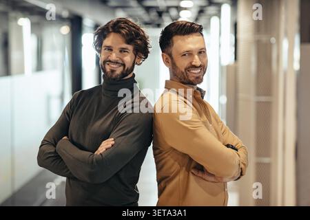 Two Smiling Men Standing Back To Back In Modern Office, Business Concept Stock Photo
