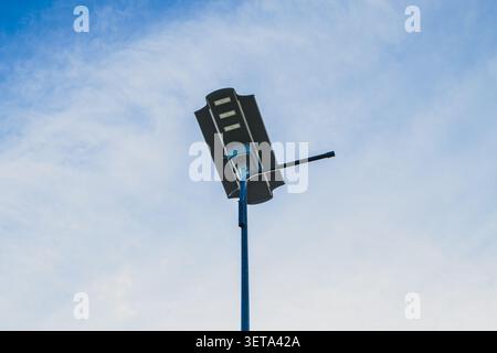 A low-angle, medium shot of an integrated all-in-one LED solar street lamp mounted on a metal pole against a clear blue sky with light wispy clouds. Stock Photo