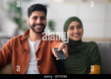 Happy Multiracial Couple Watching Television Together At Home, Smiling With Remote Control Stock Photo
