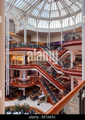 Multi-level interior of Princes Square, a shopping centre featuring a glass-domed atrium, escalators, and retail storefronts. Stock Photo
