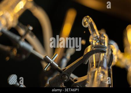 Laboratory glassware, metal clamp, and tubing in scientific distillation setup with warm lighting, highlighting precision and focus in chemical or alc Stock Photo