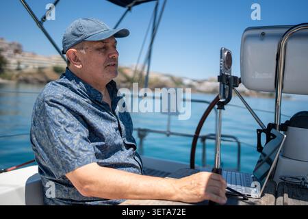 Man working remotely on sailboat using laptop smartphone Stock Photo