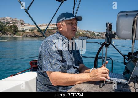 Man vlogging on sailboat while working remotely on laptop Stock Photo