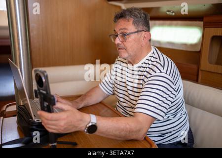 Senior man working remotely from laptop on sailboat Stock Photo