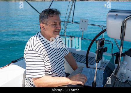 Man working remotely on sailboat by open ocean Stock Photo