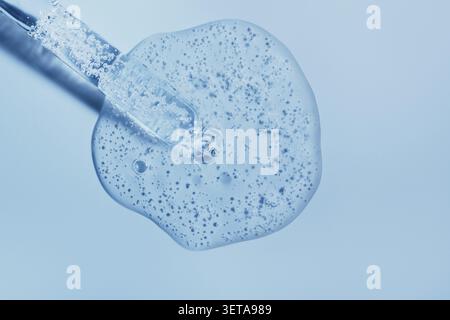 Pipette skin care gel serum with soap bubbles on blue surface Stock Photo