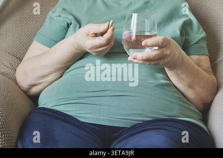 Elderly woman taking medication with a glass of water for health and wellbeing Stock Photo