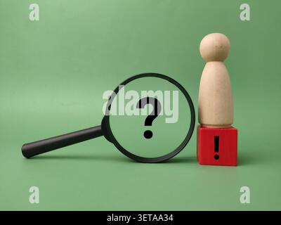 A black magnifying glass frames a question mark next to a wooden figure standing on an exclamation mark block. Stock Photo