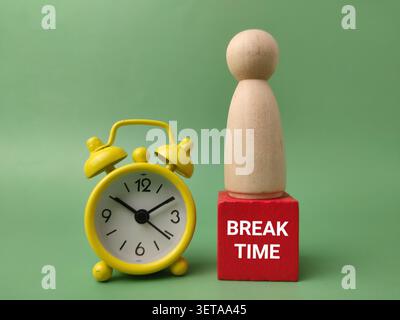 A wooden peg figure stands on a red block reading BREAK TIME next to a yellow alarm clock. Stock Photo