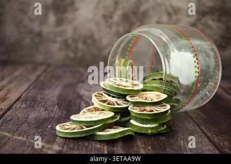 Dried lime slices spill from a jar on a wooden table Stock Photo