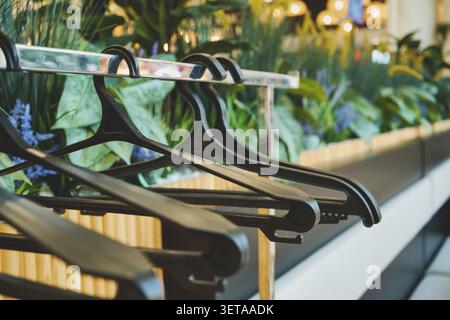 Empty black plastic clothes hangers hanging on a sales rack with green plants in the background Stock Photo